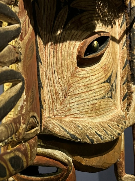 Intrication d'un masque en bois avec des détails fins et une représentation stylisée de l'œil.