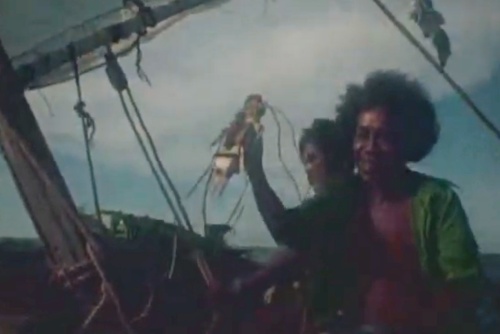 Deux personnes sur un bateau, l'une tenant une lanterne et l'autre souriant, sous un ciel nuageux.
