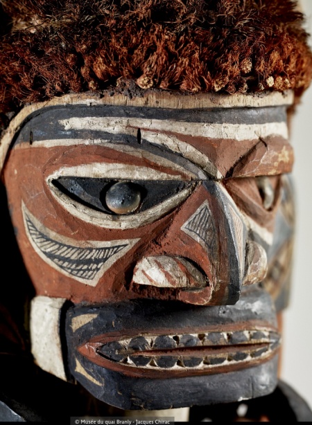 Masque en bois sculpté avec des éléments décoratifs, représentant un visage humain, avec des traits stylisés et des yeux en verre.