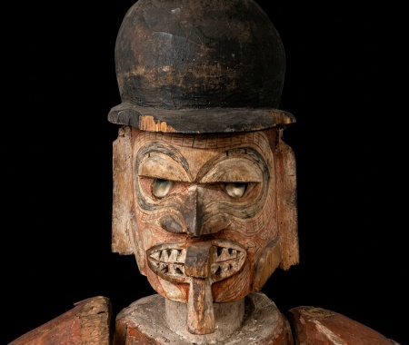 Masque en bois représentant une figure humaine avec un chapeau haut de forme.